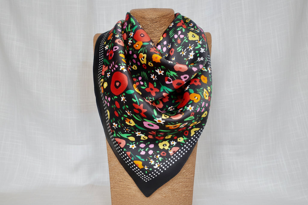 Night floral silk scarf styled on mannequin showing luxurious drape and vibrant multicolor botanical print with red yellow pink flowers on black silk