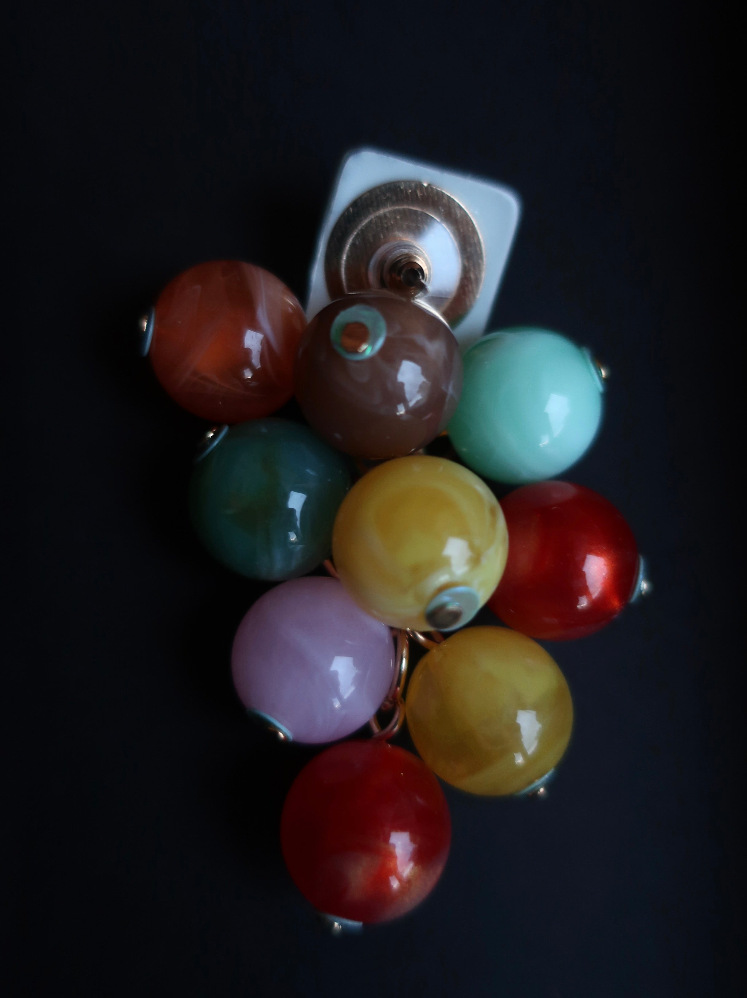 A cluster of colorful glass bead earrings with gold-toned metal settings, displayed on a solid black background.