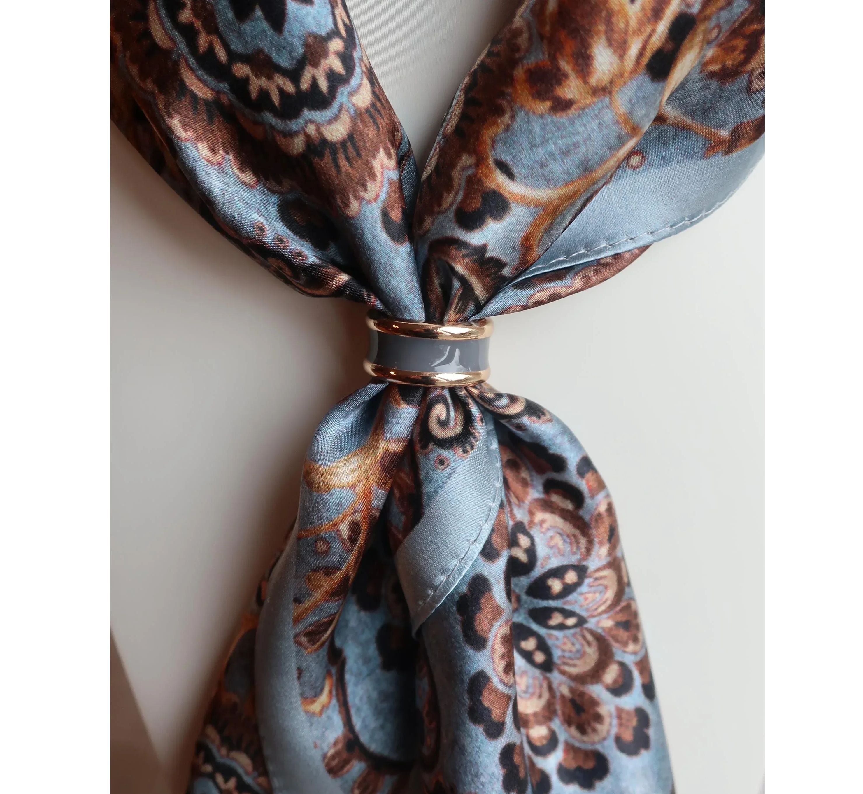 Patterned scarf tied in a knot with a decorative ring on a light background