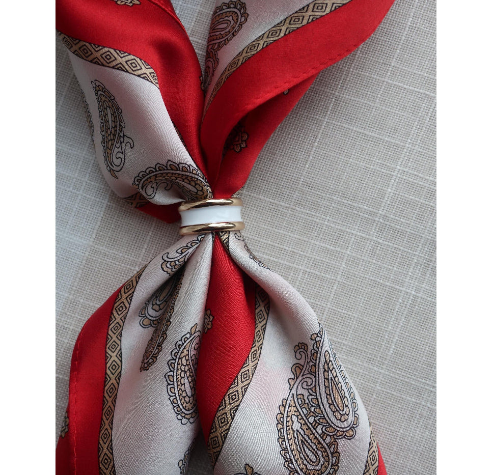 Red and grey paisley mulberry silk scarf styled with a gold and white enamel scarf ring, elegantly folded on a linen background